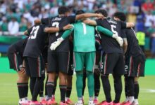 Vista trasera de los jugadores de la Selección Mexicana de fútbol masculino durante la Copa Mundial de la FIFA 2026, luciendo su tercer uniforme de color negro con sutiles detalles en verde y rojo, y el portero con indumentaria verde, todos reunidos en un círculo abrazados sobre la cancha antes de iniciar el partido.