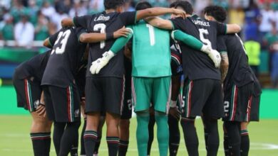 Vista trasera de los jugadores de la Selección Mexicana de fútbol masculino durante la Copa Mundial de la FIFA 2026, luciendo su tercer uniforme de color negro con sutiles detalles en verde y rojo, y el portero con indumentaria verde, todos reunidos en un círculo abrazados sobre la cancha antes de iniciar el partido.