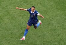 El futbolista francés Kylian Mbappé, vistiendo el uniforme azul de su selección con el número 10, corre sonriente sobre el césped verde con los brazos extendidos para celebrar un gol.