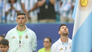 El portero Emiliano "Dibu" Martínez mira al frente con seriedad mientras Lionel Messi levanta la cabeza con los ojos cerrados durante un partido de la selección argentina.