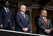 Gianni Infantino, presidente de la FIFA, de pie en un palco presidencial junto a otros directivos del fútbol internacional vistiendo trajes formales.