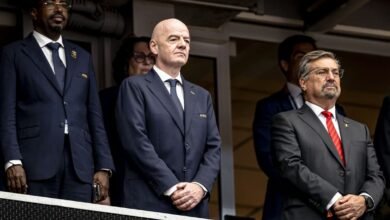 Gianni Infantino, presidente de la FIFA, de pie en un palco presidencial junto a otros directivos del fútbol internacional vistiendo trajes formales.