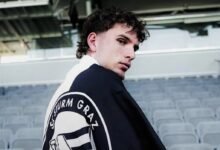 Luis Balbo de espaldas mostrando el escudo del SK Sturm Graz impreso en su chaqueta dentro del estadio