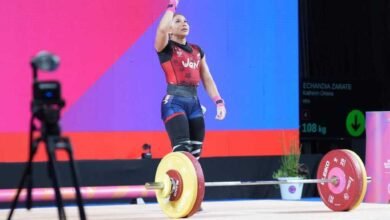 Fotografía de la pesista venezolana Katherin Echandía celebrando sobre la tarima de levantamiento de pesas. Viste un traje de halterofilia en colores rojo, azul y negro con la palabra "Ven" en el pecho. La atleta levanta el brazo derecho apuntando hacia el cielo en señal de victoria frente a una barra cargada con discos Eleiko de color amarillo y rojo.