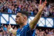 El futbolista venezolano Kevin Kelsy celebra con los brazos abiertos frente a la afición, vistiendo la camiseta azul del Rangers F.C. en el estadio de Ibrox.