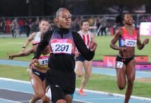 En primer plano y destacada en el centro, la velocista Orangys Jiménez (con el dorsal 291 en el pecho) corre con intensidad vistiendo uniforme negro de manga larga. A su derecha, se observa a la atleta ecuatoriana Nicole Caicedo (con el dorsal 223) y, al fondo a la izquierda, otras corredoras rezagadas completando la prueba en una pista azul.