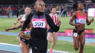 En primer plano y destacada en el centro, la velocista Orangys Jiménez (con el dorsal 291 en el pecho) corre con intensidad vistiendo uniforme negro de manga larga. A su derecha, se observa a la atleta ecuatoriana Nicole Caicedo (con el dorsal 223) y, al fondo a la izquierda, otras corredoras rezagadas completando la prueba en una pista azul.