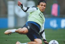El defensor venezolano Jon Mikel Aramburu se barre sobre el césped mojado para alcanzar un balón durante un entrenamiento con la Real Sociedad, vistiendo indumentaria deportiva negra y un peto amarillo.