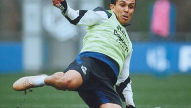 El defensor venezolano Jon Mikel Aramburu se barre sobre el césped mojado para alcanzar un balón durante un entrenamiento con la Real Sociedad, vistiendo indumentaria deportiva negra y un peto amarillo.